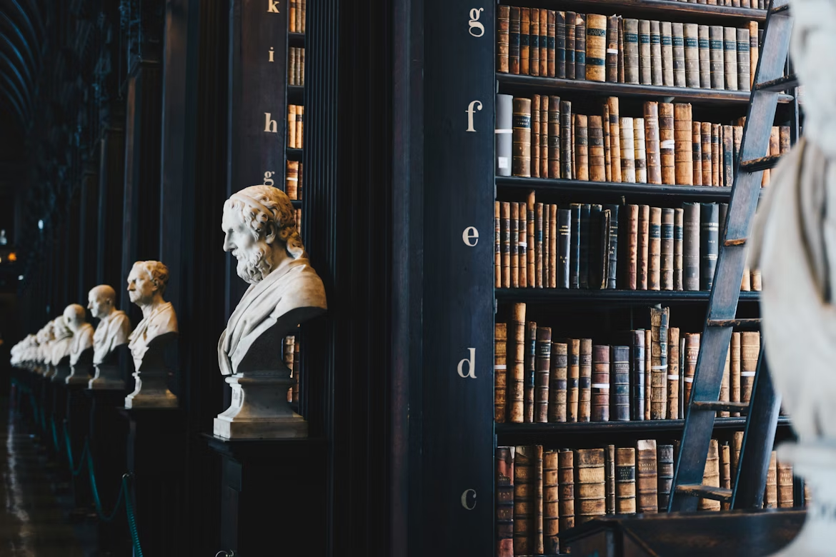 Books on black wooden shelves with marble busts.