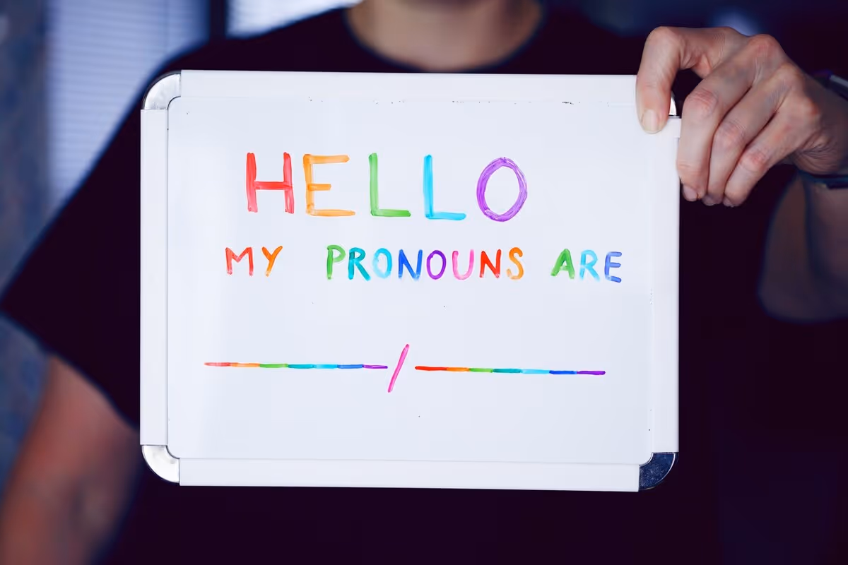 An image of a person holding out a whiteboard that says “Hello my pronouns are” followed by a blank space.