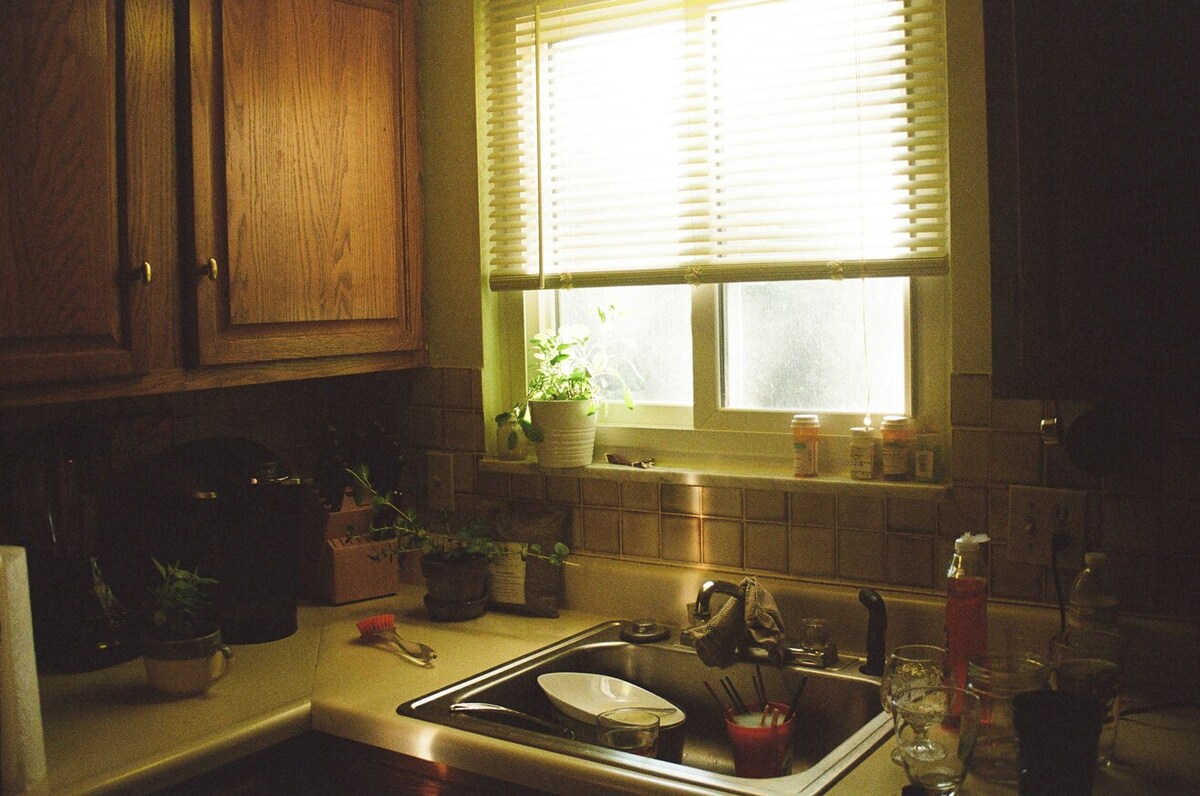 A messy kitchen area, with dishes in the sink and empty glasses on the counter.