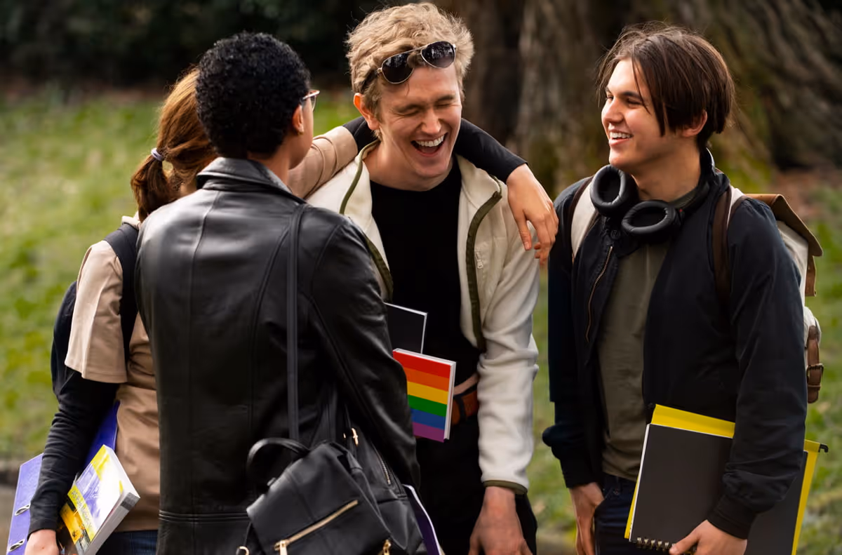 Four young people are engaged in conversation, laughing and enjoying each other's company outdoors.  
