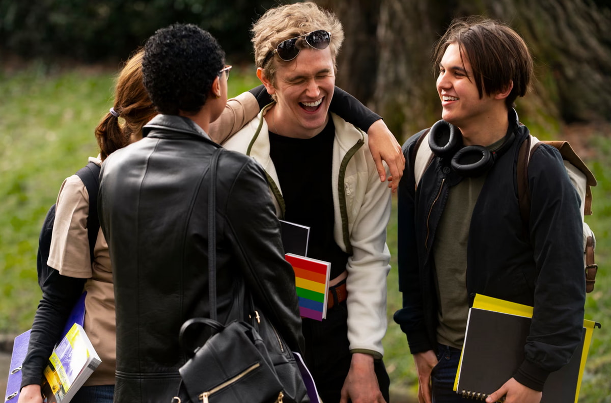Four young people are engaged in conversation, laughing and enjoying each other's company outdoors.  