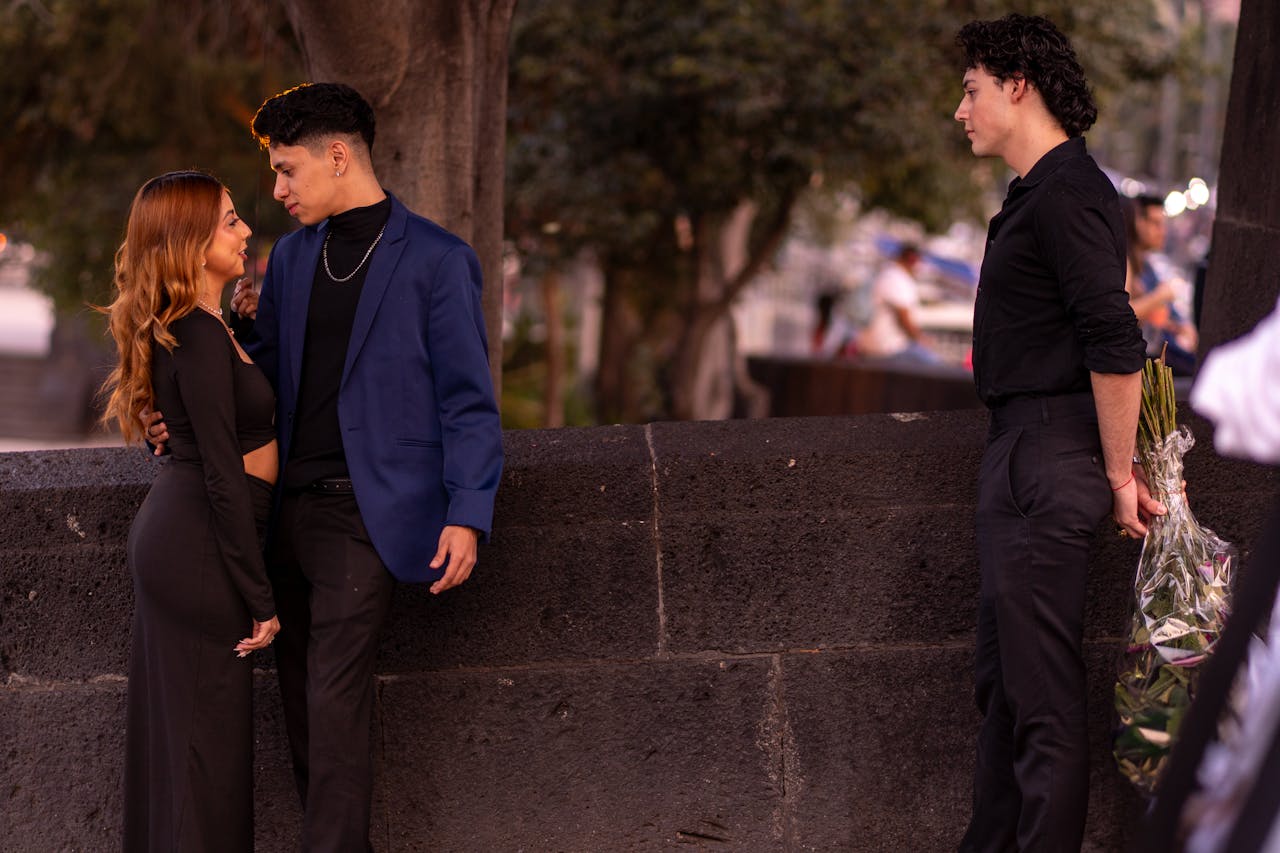 friend standing off to the side as a couple stands close together, smiling and laughing together