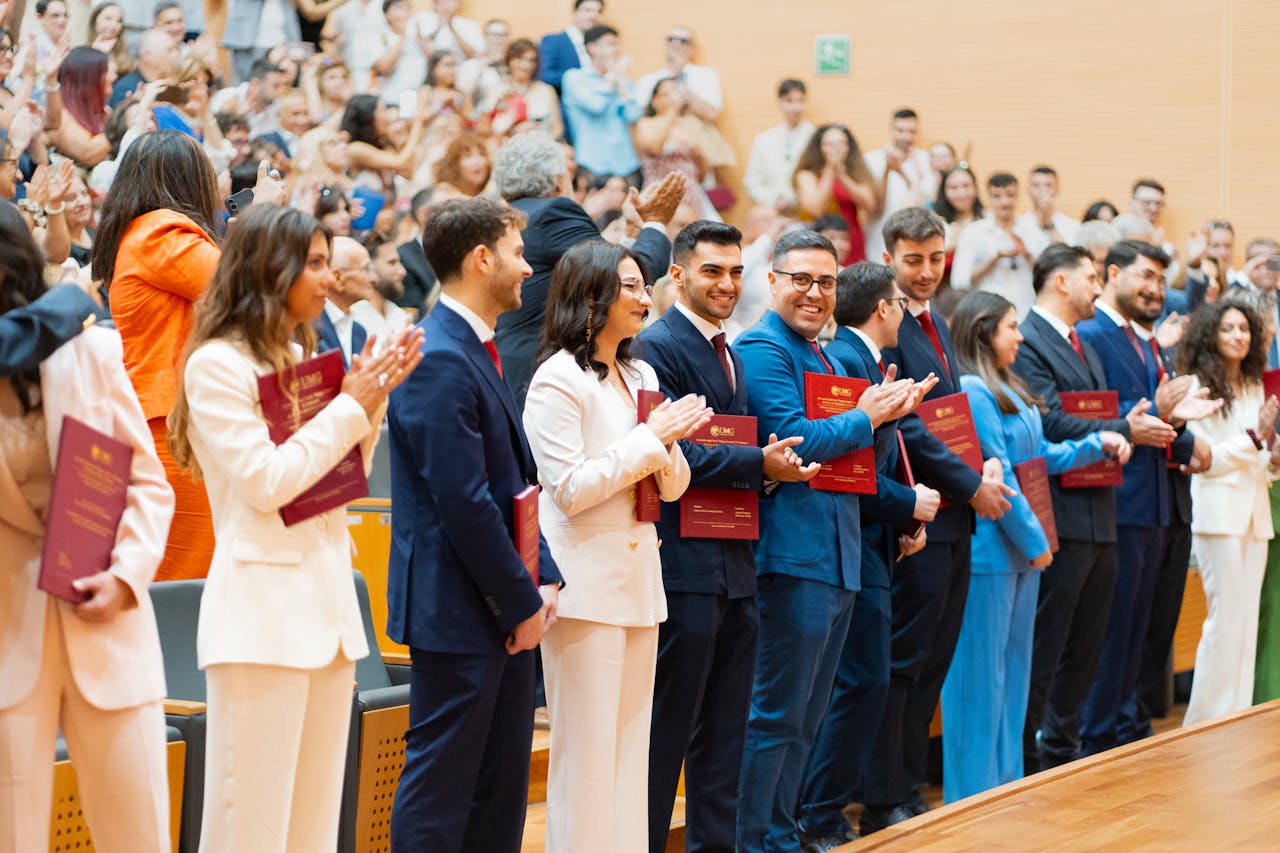 MBA students wearing business attire standing in a row and clapping at a graduation ceremony