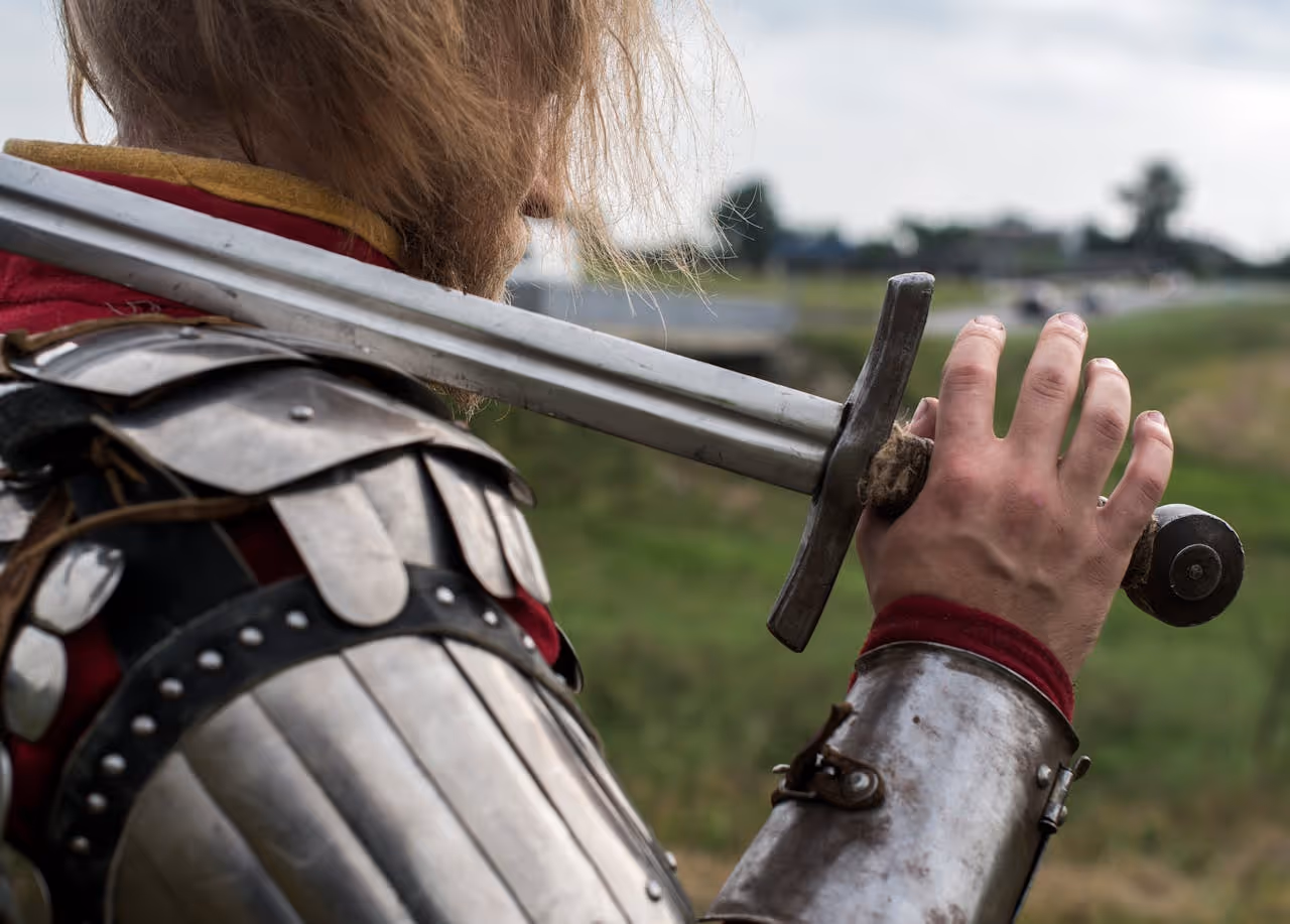 close up of a knight with a sword resting on his shoulder and his hand on the hilt