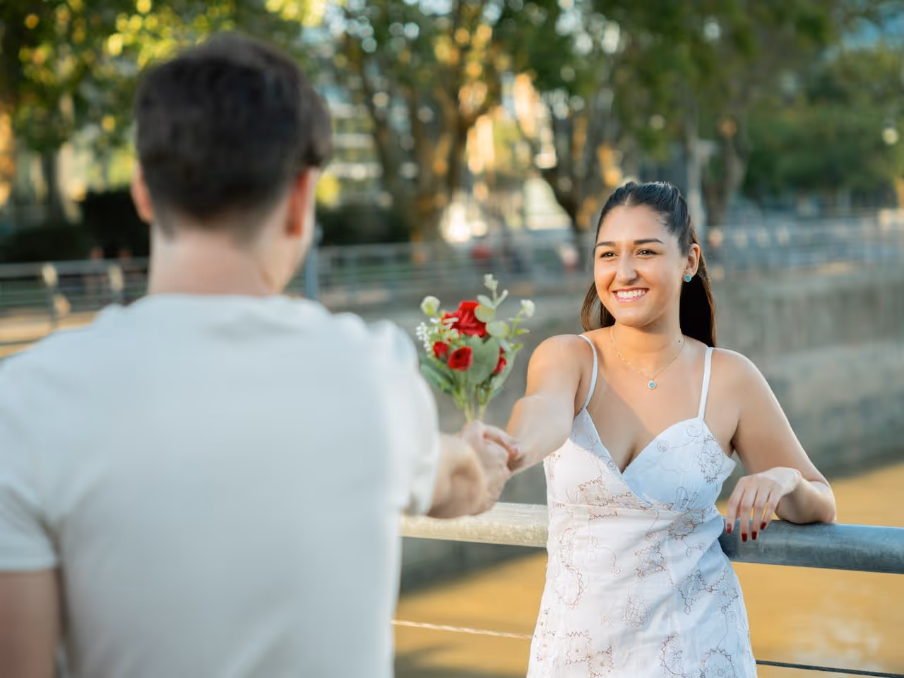couple holding a boquet of roses between them so that it's unclear who is handing the flowers to whom