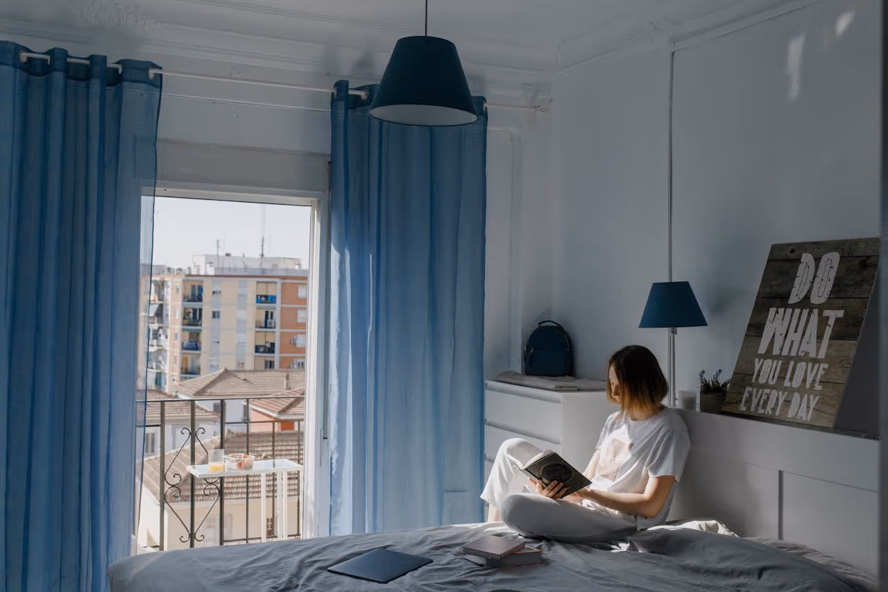 woman reading in the bedroom of her first apartment with the windows open to the city