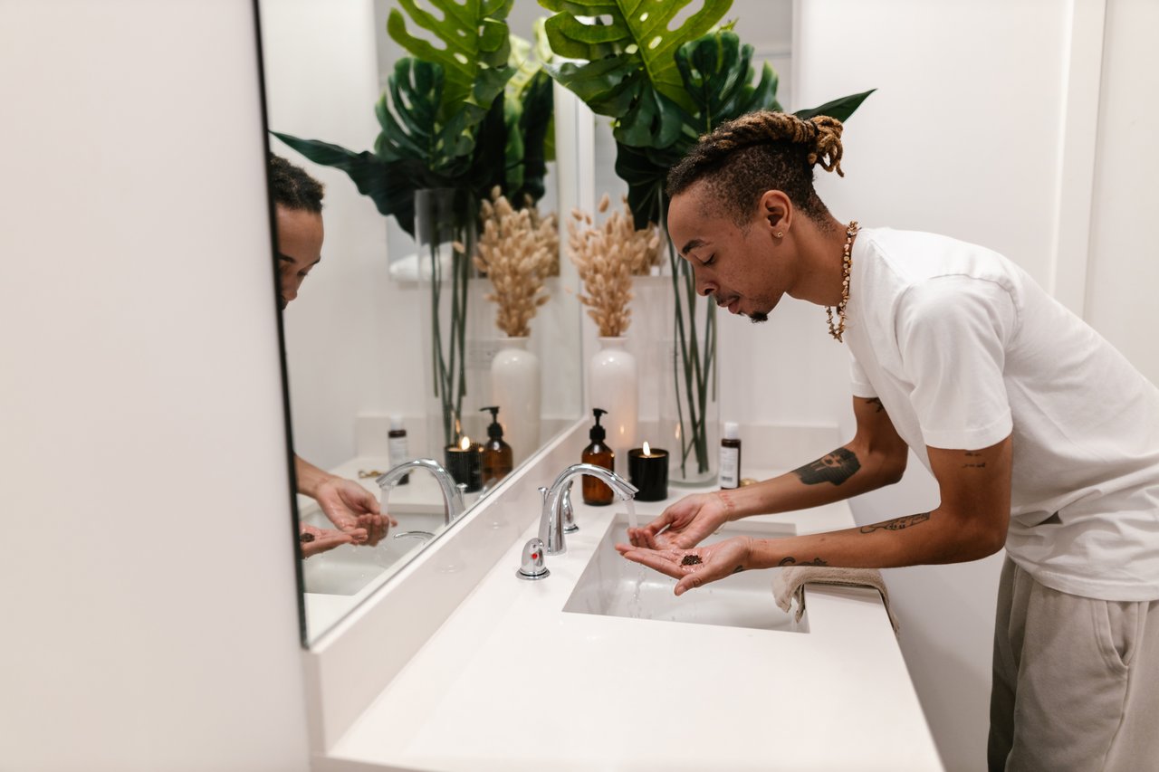 man washing his face in the sparkling clean bathroom of his first apartment
