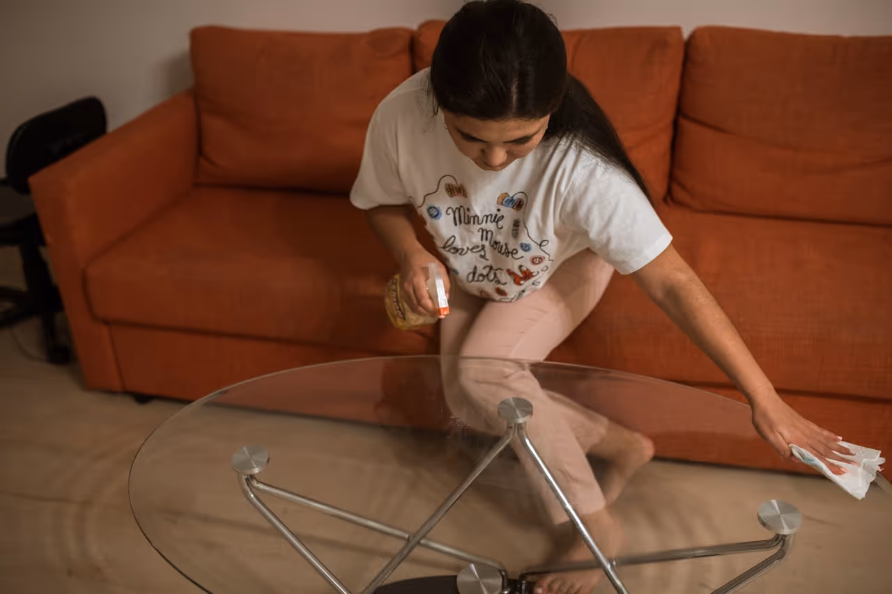 college student wiping down a class coffee table with a paper towel and cleaning spray
