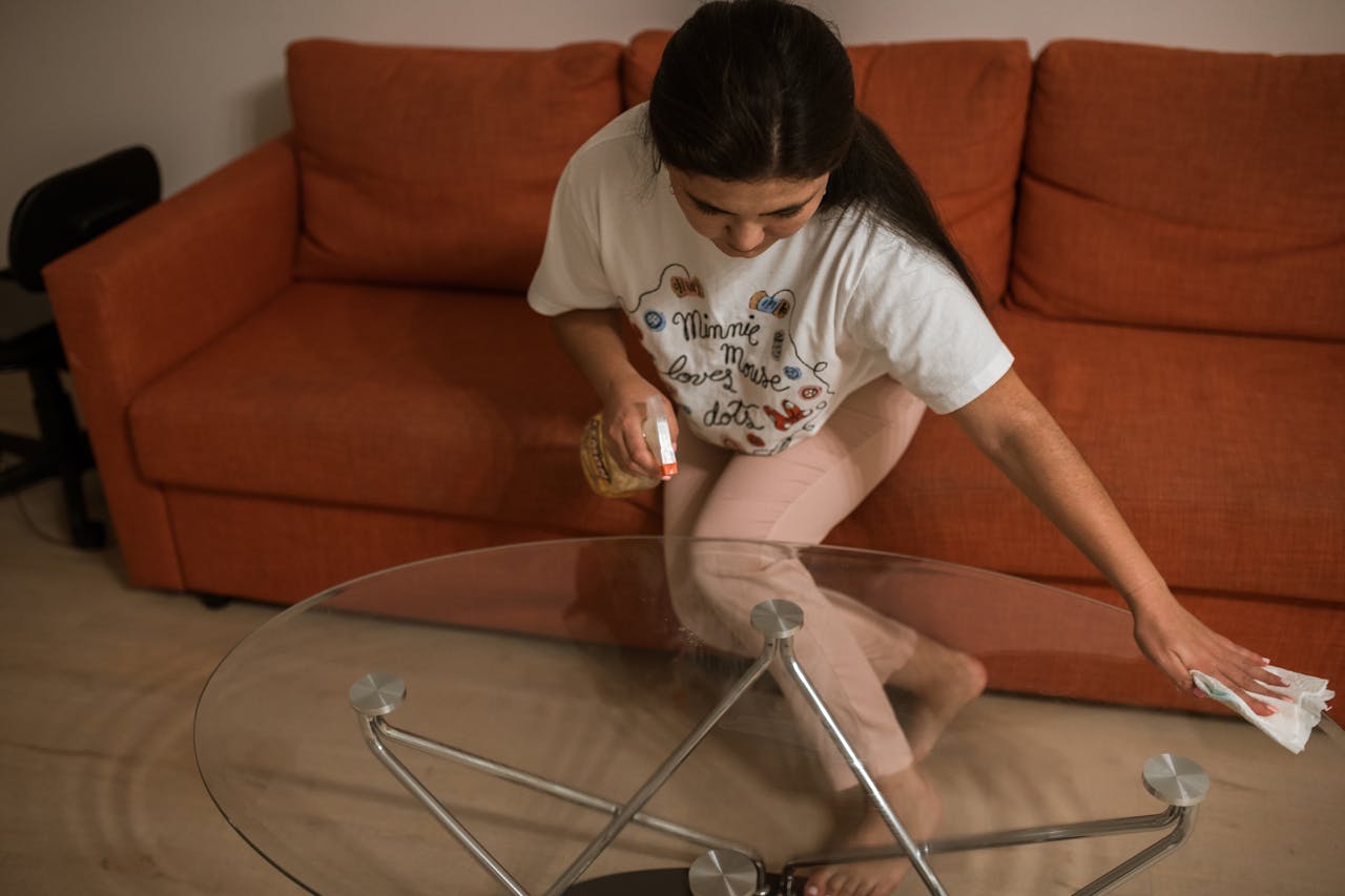 college student wiping down a class coffee table with a paper towel and cleaning spray