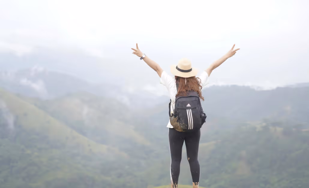 20something on a solo trip for the first time standing on top of the mountain, thrilled at the adventure