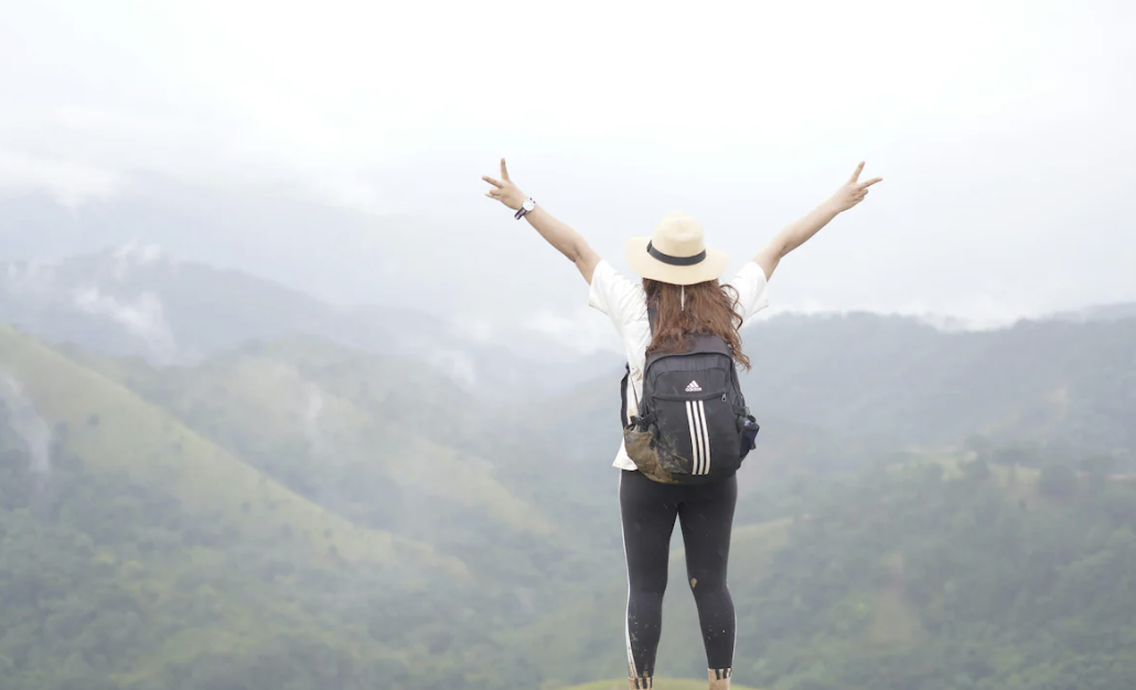 20something on a solo trip for the first time standing on top of the mountain, thrilled at the adventure