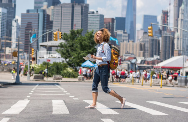 woman marching across a crosswalk, map in hand, in New York City