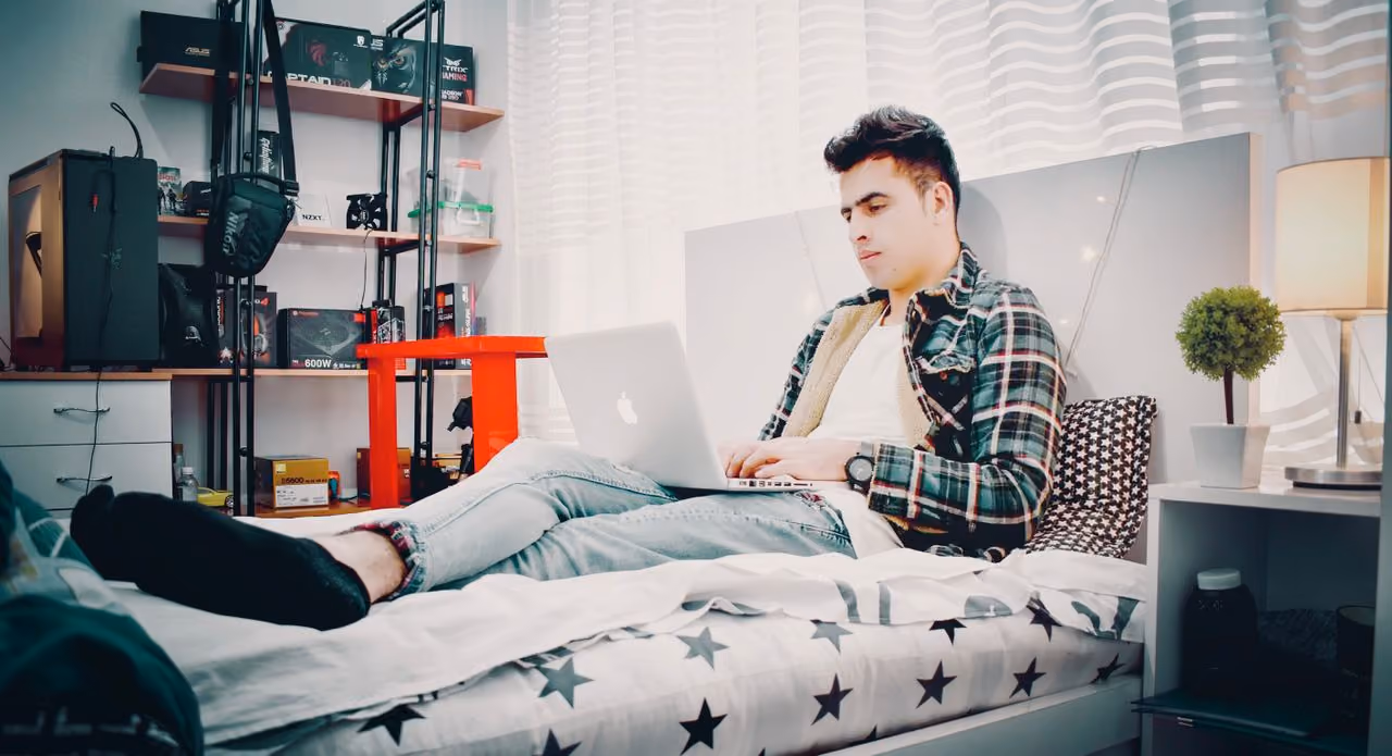 college student working on his laptop in his comfortably made twin xl bed