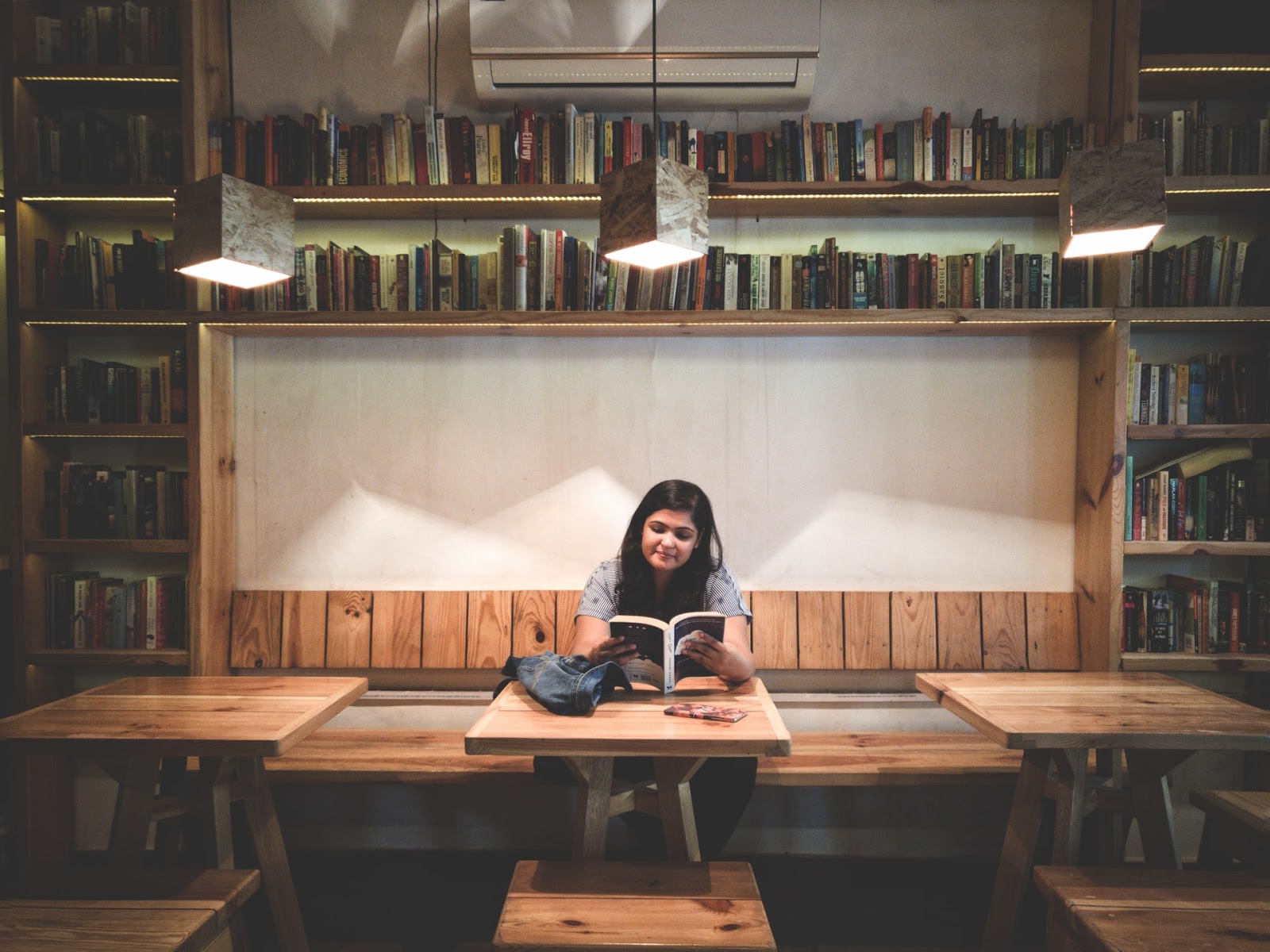 20something reading at a table in a coffee shop surrounded by book shelves