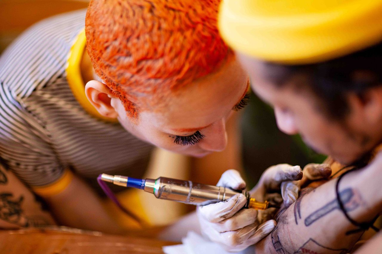 tattoo artist with short orange hair inking a man in his 30s