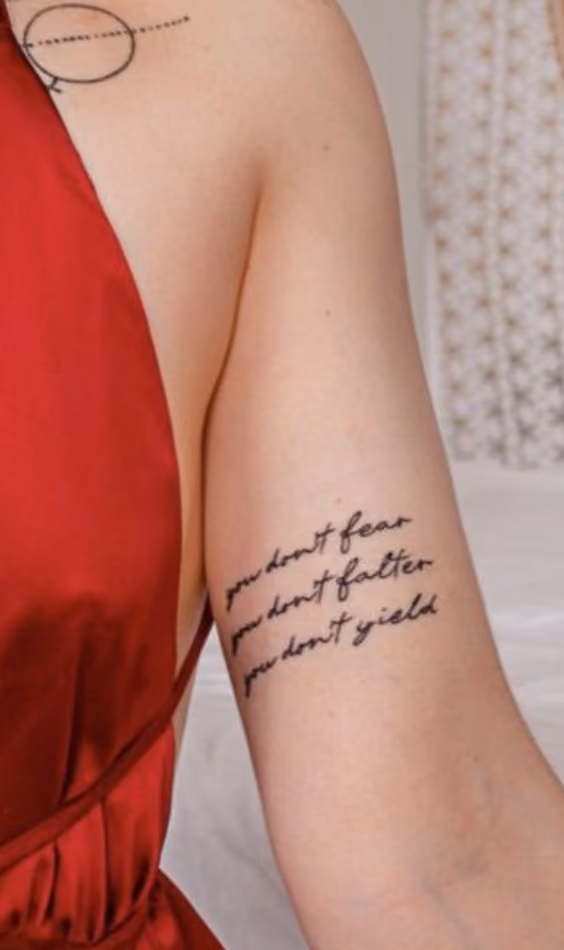 You do not fear. You do not falter. You do not yield. Throne of Glass mental health tattoo on the forearm of a woman in a red satin dress