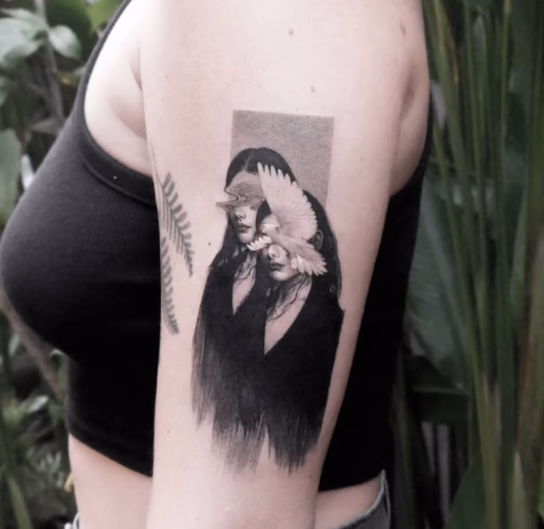 woman with an upper arm tattoo featuring two portraits of girls, one whose face is obscured by an abstract swirl and the other whose face is hidden by a dove in flight