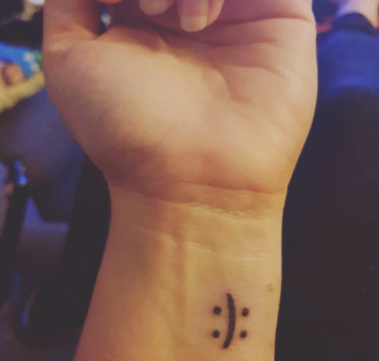 wrist tattoo that's a simple left paranthesis with a colon on either side, so it can form a smiling or frowning emoticon depending on how you look at it, like an internet-age face of Janus