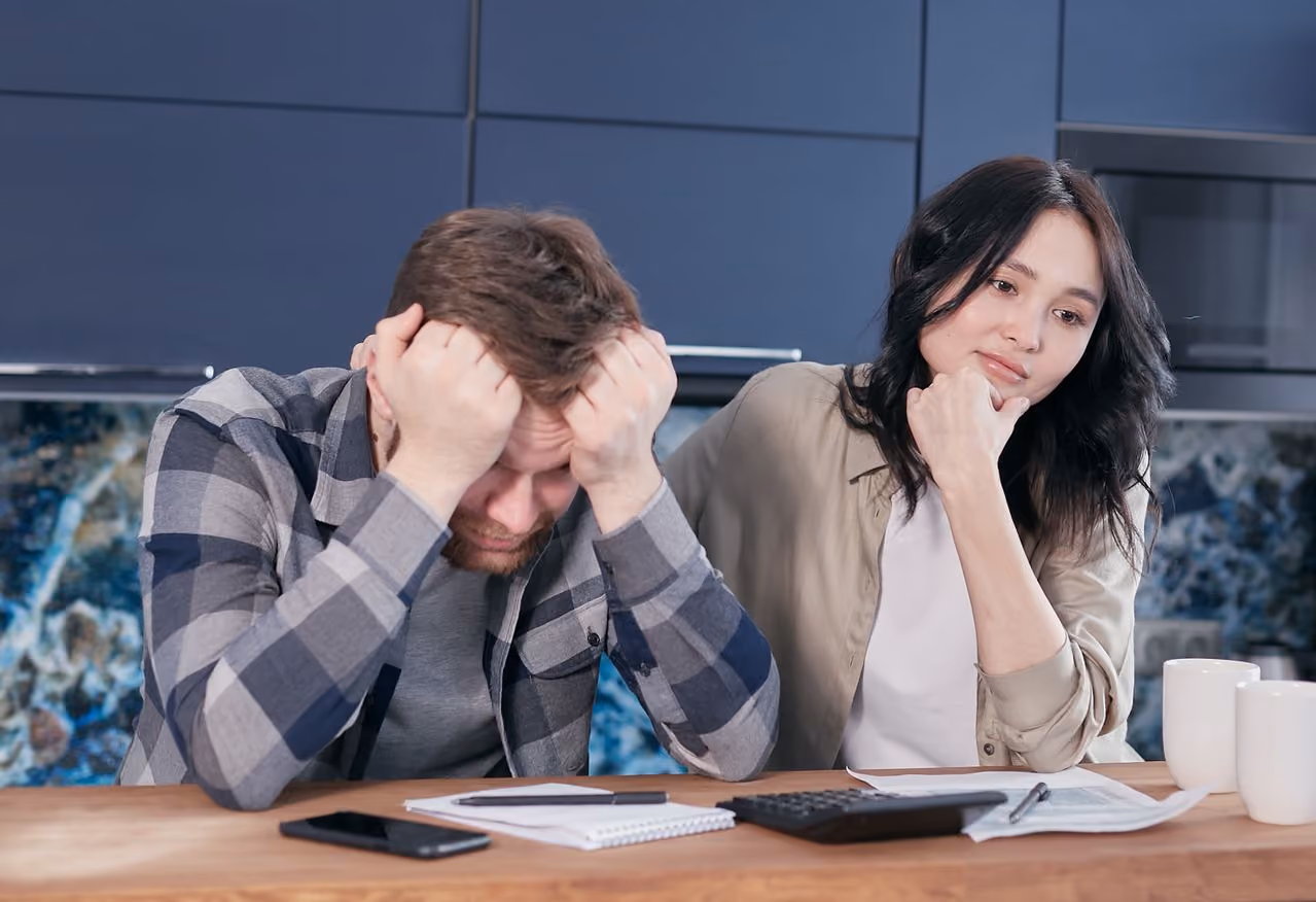 couple sitting at their table with financial document spread around looking stressed out about finding the money to invest in retirement when the budget already feels tight