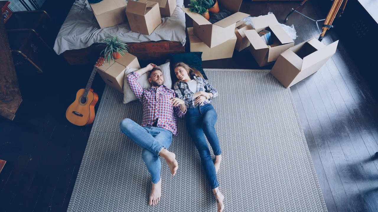 couple lying on the floor surrounded by moving boxes after making the leap from long distance to living together