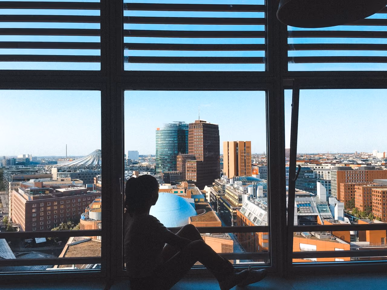 woman who moved for love looking out the window at a city, feeling adrift and alone
