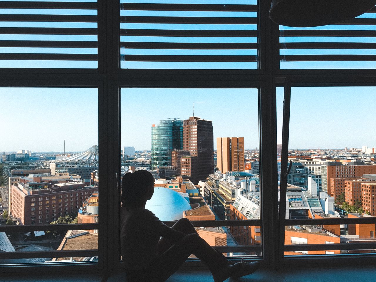 woman who moved for love looking out the window at a city, feeling adrift and alone