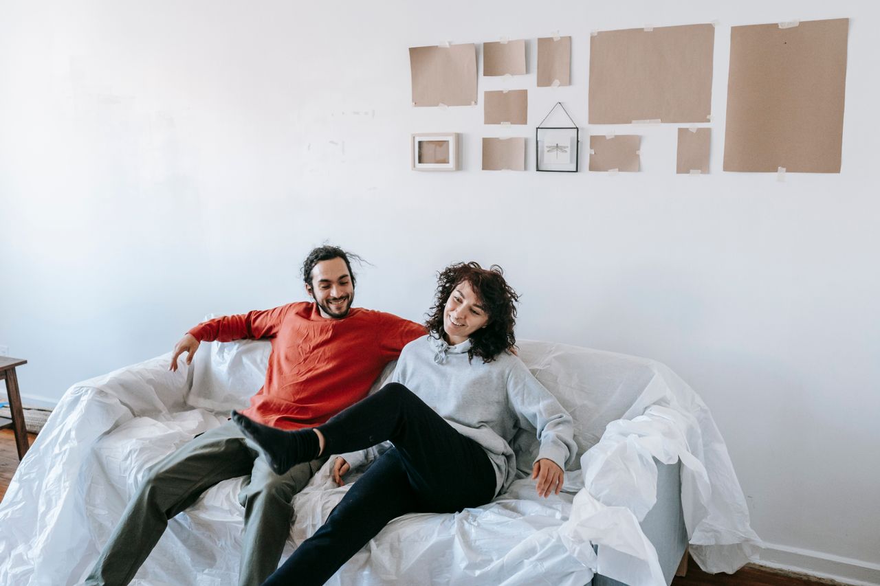 couple sitting on a sofa together in their new shared apartment, laughing and looking content