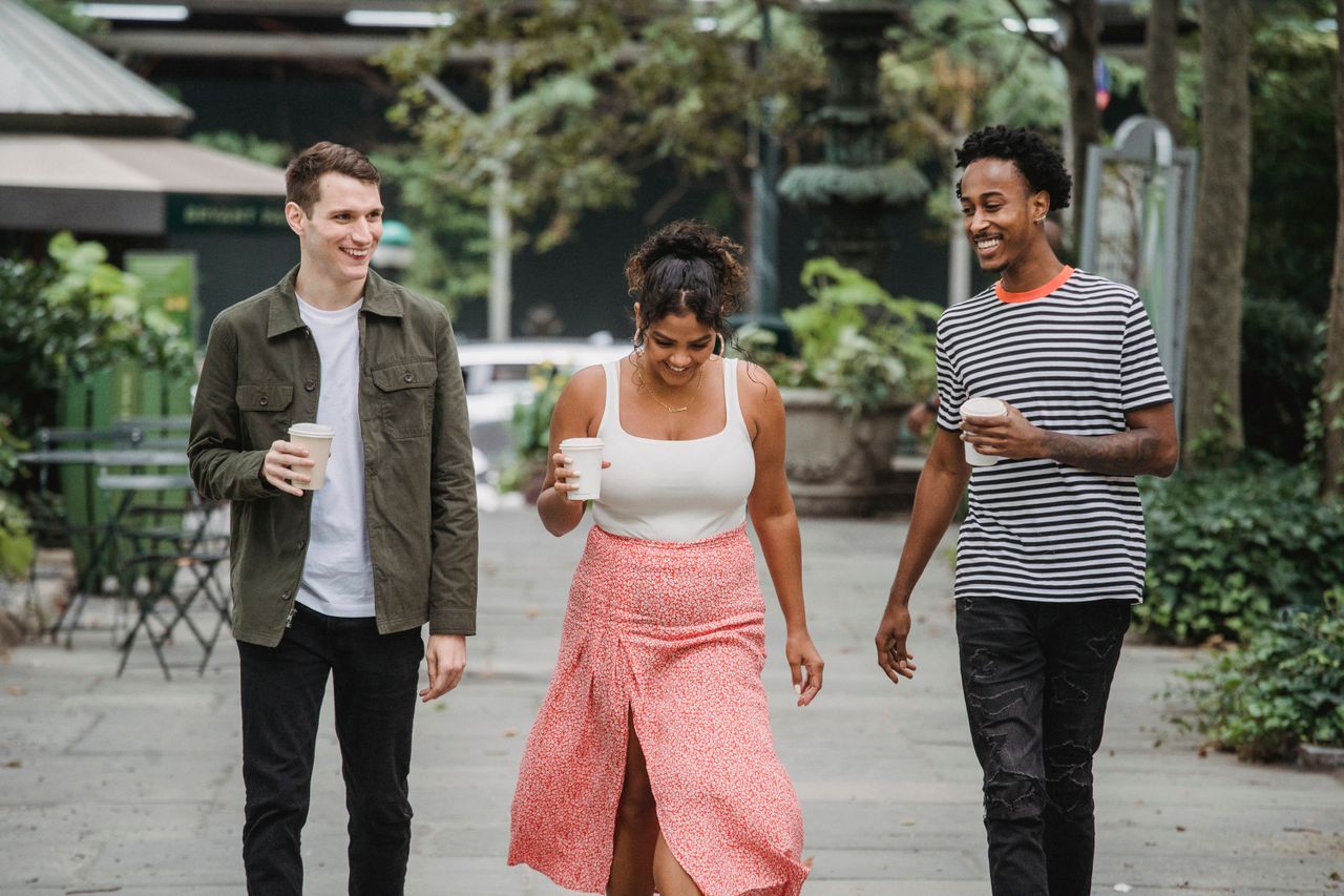 couple and a mutual friend walking down a city street holding coffees and laughing
