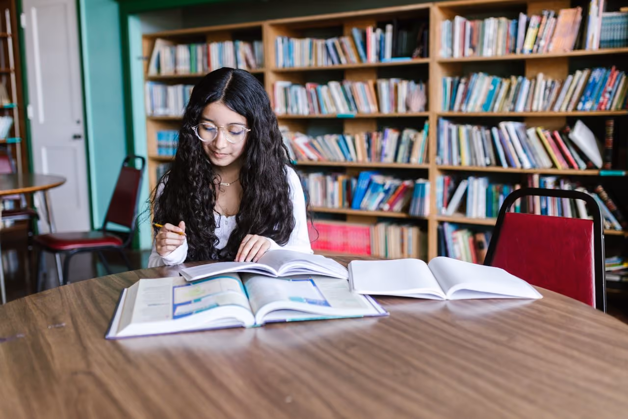 college student at the university library with a textbook and notebook open in front of her