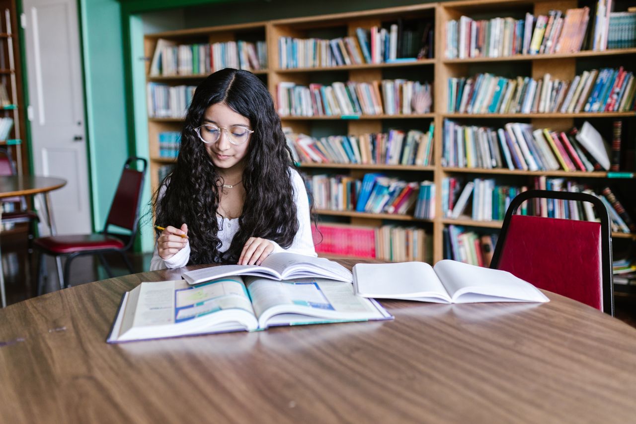 college student at the university library with a textbook and notebook open in front of her