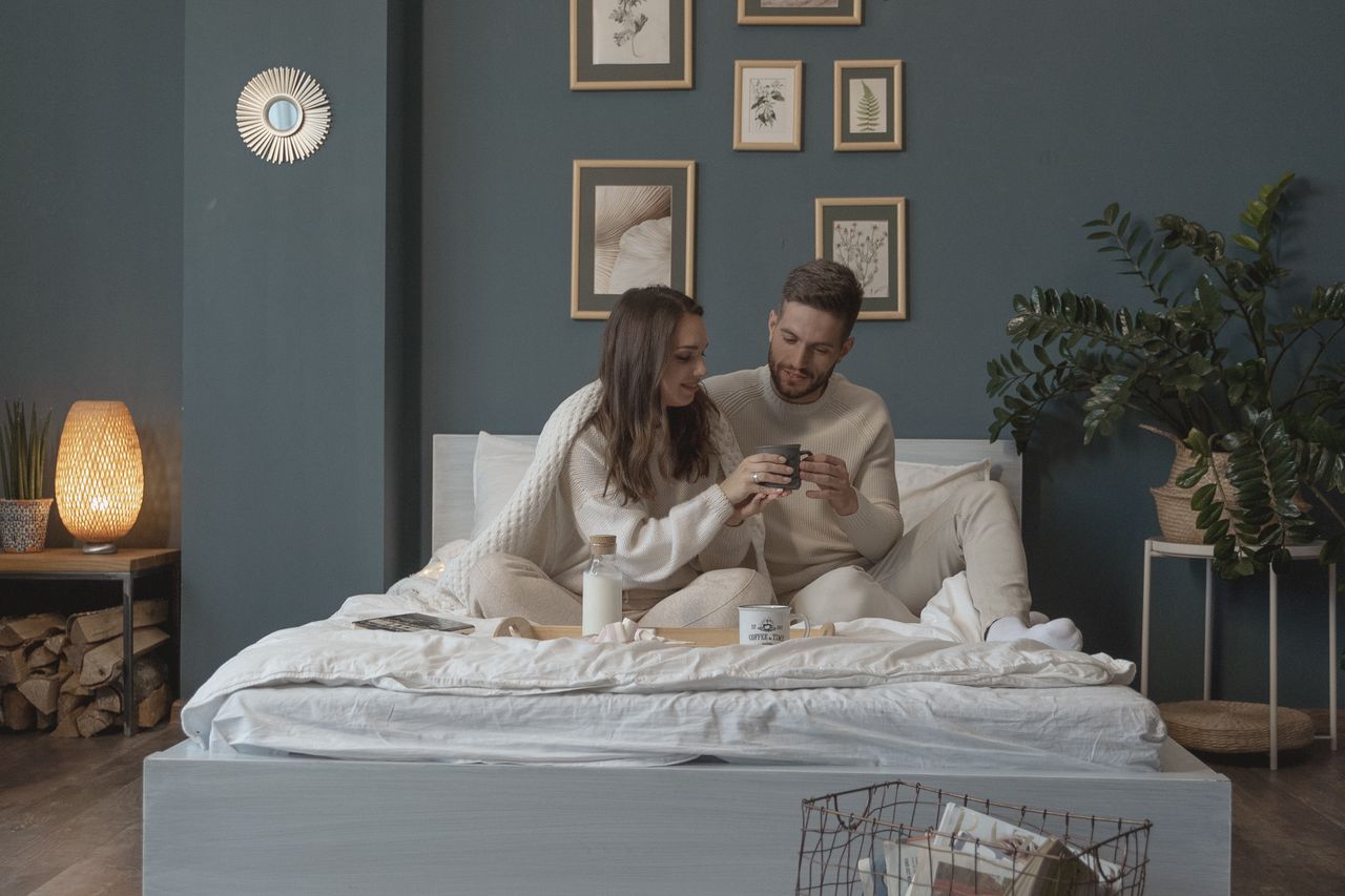 couple having a cozy day relaxing on a bed made up with pottery barn bedding alternatives to be just as comfy without costing high-end prices