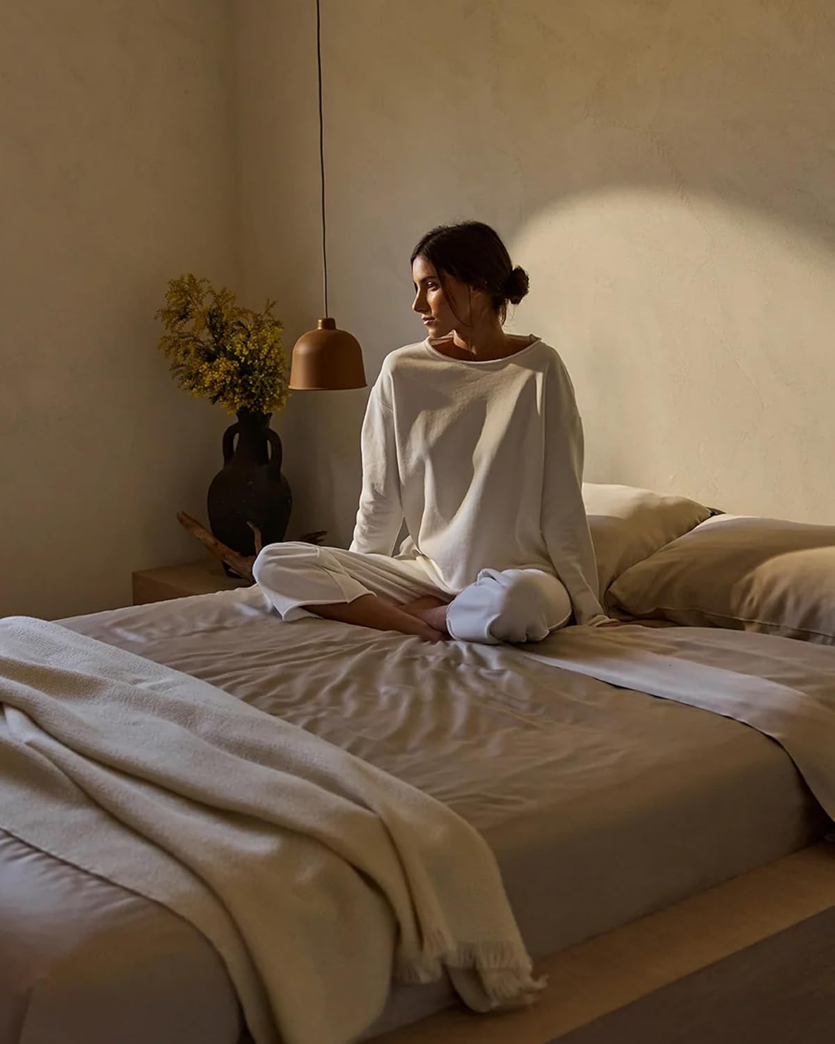 woman in a cozy, earth-toned bedroom relaxing on a cooling bamboo comforter