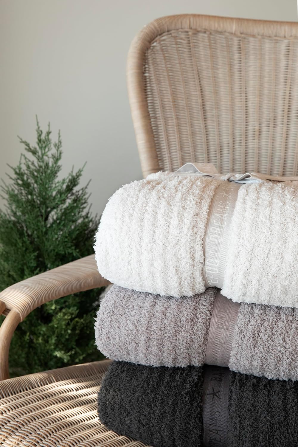 CozyChic throw blankets folded and stacked on a wicker chair giving a soft opulence to the bedroom any fan of the Pottery Barn aesthetic would appreciate