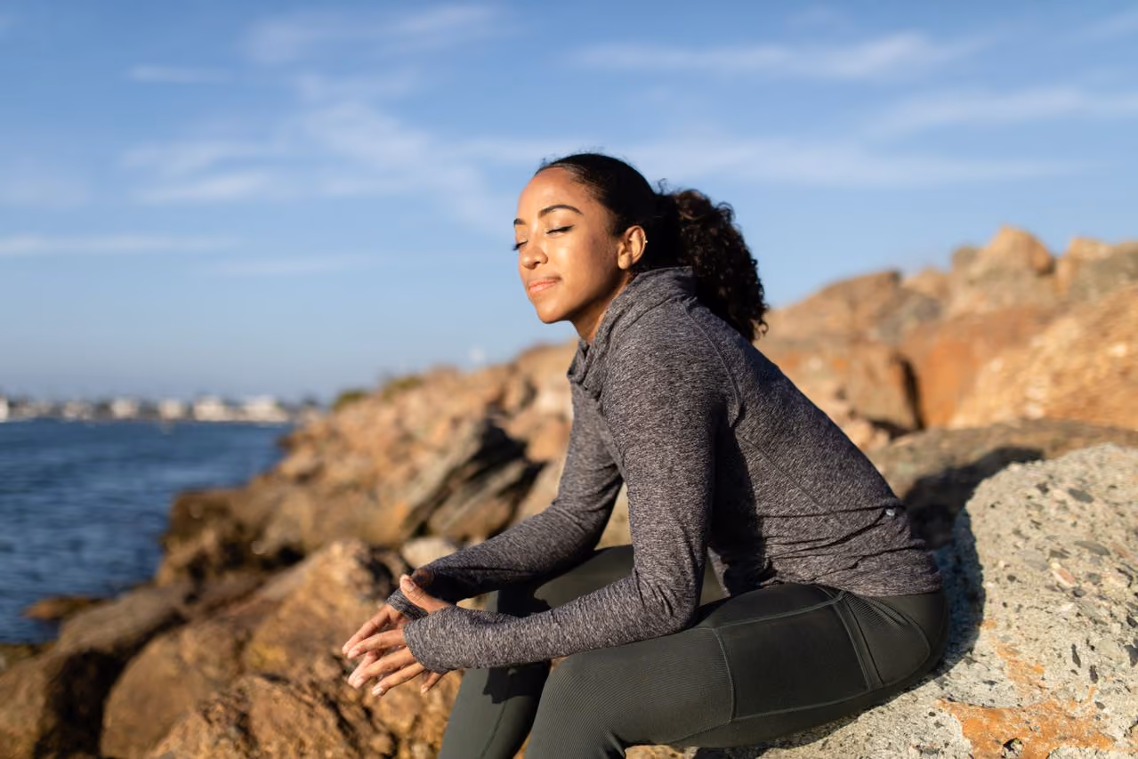 woman wearing athletic clothes resting during a beach workout, smiling because she's wearing affordable Vuori alterntives