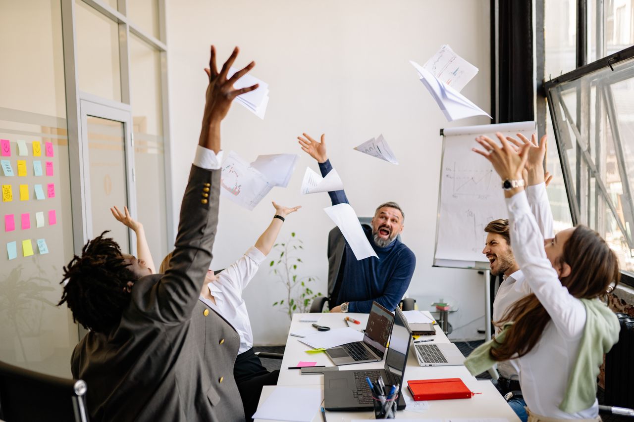work team gathered around a table throwing papers in the air in celebration