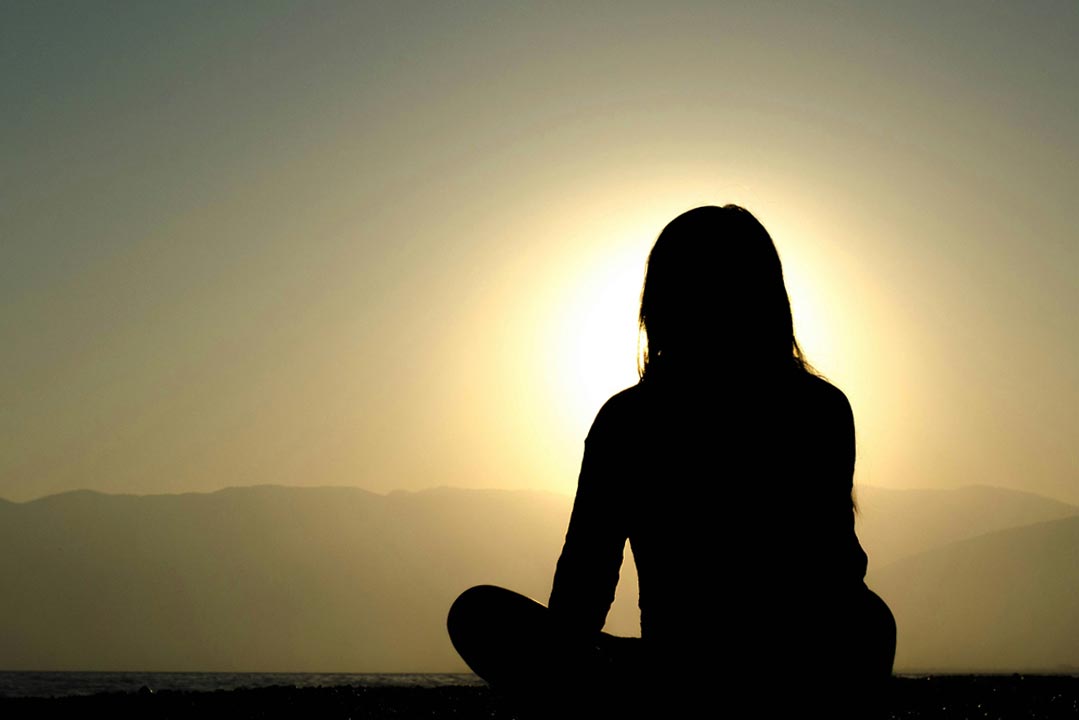 Woman meditating in nature on a mountain peak, finding inner peace through mindfulness and deep breathing techniques to reduce anxiety