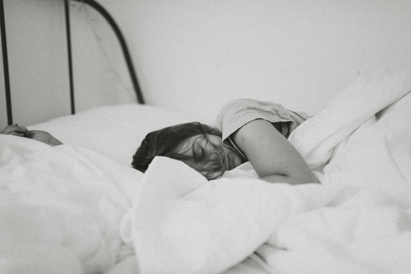 Peaceful woman sleeping in a cozy bed, representing the importance of a calming sleep routine for anxiety relief