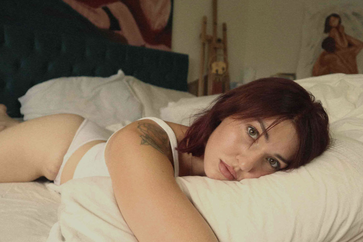 Gia lying on the bed in underwear and socks, making eye contact with the camera – celebrating body confidence and natural beauty.