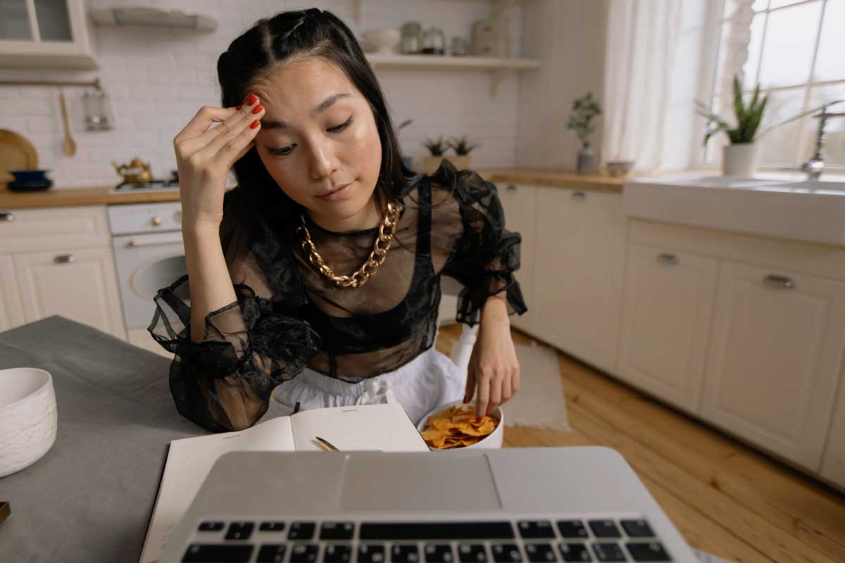Asian woman holding her head in frustration during a Zoom video call, showing signs of virtual meeting anxiety.
