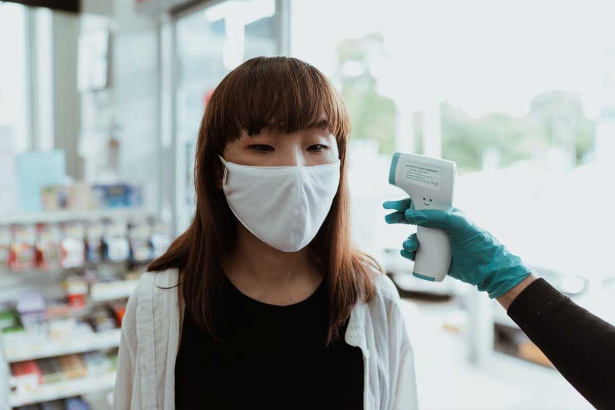 Asian girl wearing a face mask getting her temperature checked with a no-contact thermometer gun, health safety measure during COVID-19.