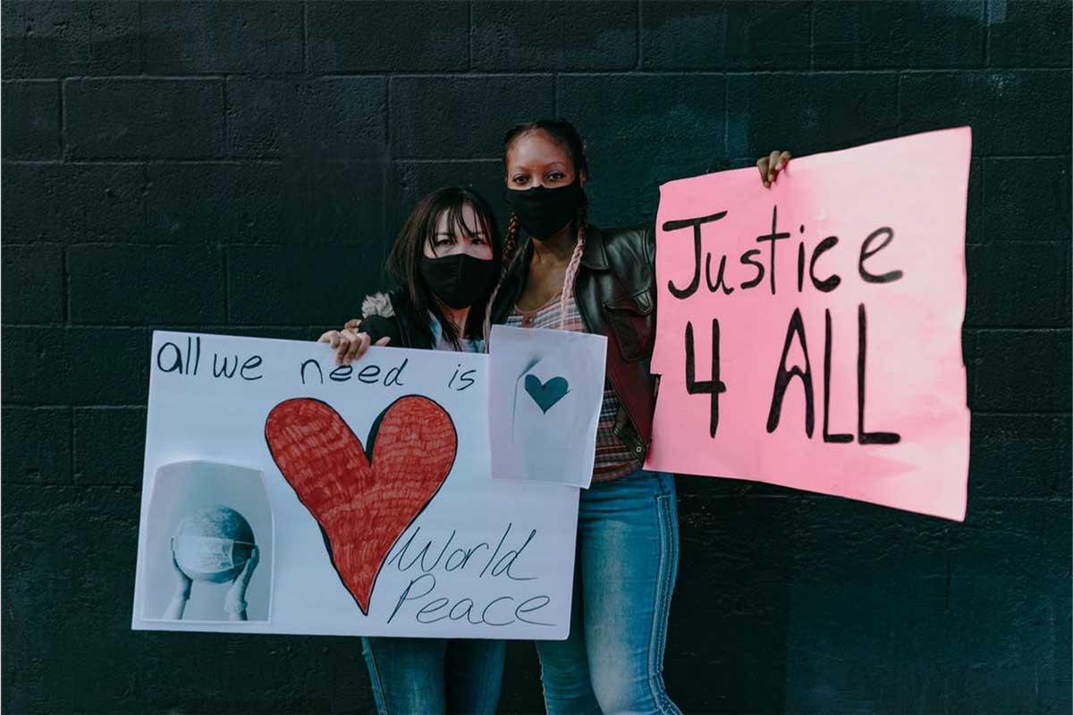 Two young women wearing face masks holding protest signs reading “Justice for All” during a peaceful demonstration for racial equality.