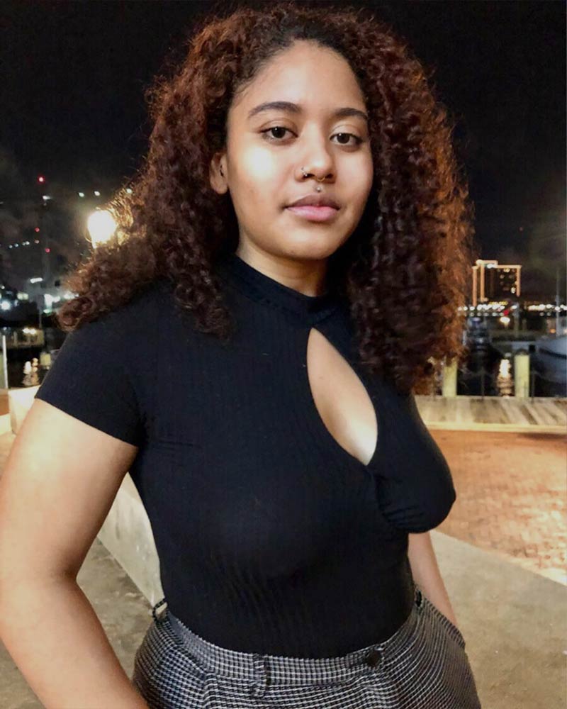Black girl with curly hair wearing a black shirt, confidently posing and embracing her natural body.