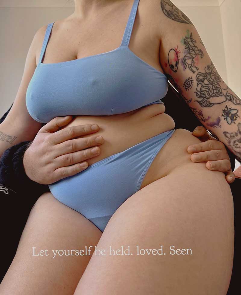 Plus-size woman in teal bra and underwear embracing her body while being supported by her boyfriend