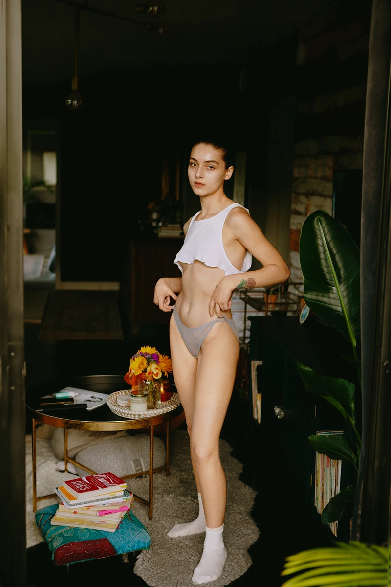 Color photograph of her standing in underwear and white tank top, slender natural body, effortless elegance