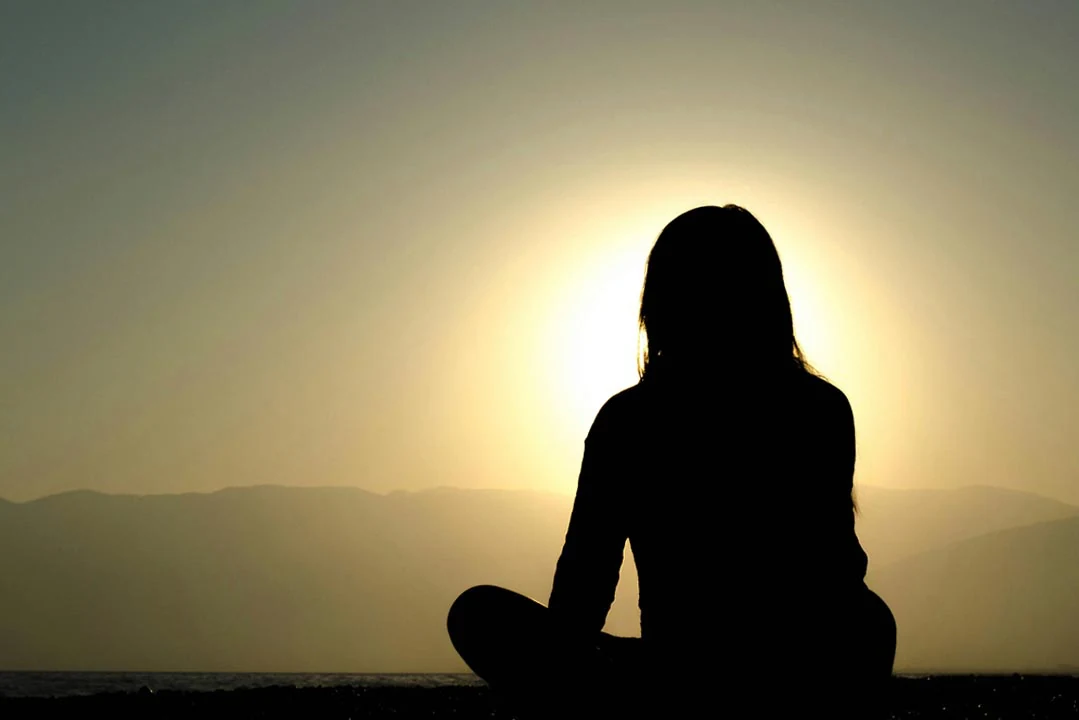 Woman meditating in nature on a mountain peak, finding inner peace through mindfulness and deep breathing techniques to reduce anxiety