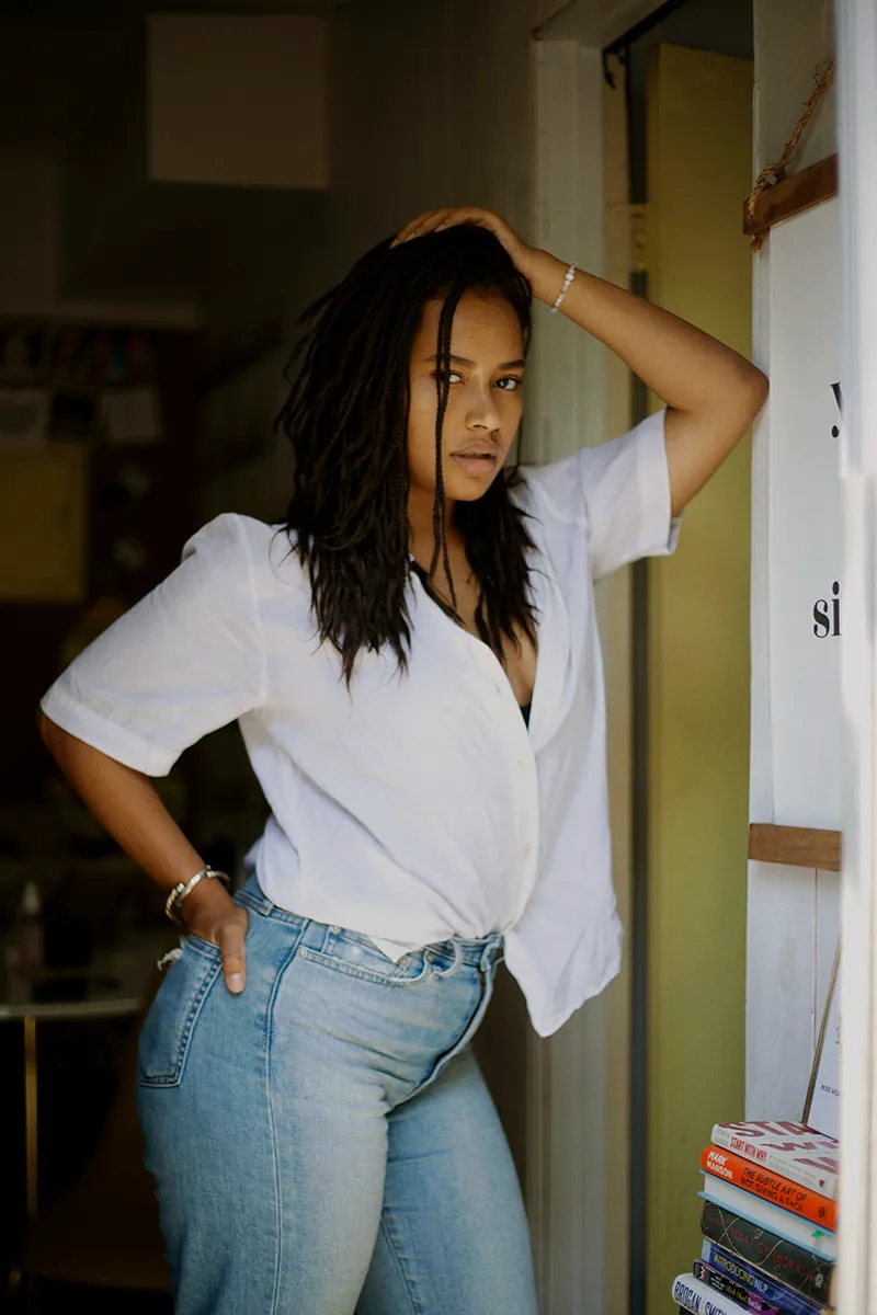 Color portrait of a young Black woman with dreadlocks, no makeup, wearing blue jeans, embracing her natural curves and beauty.