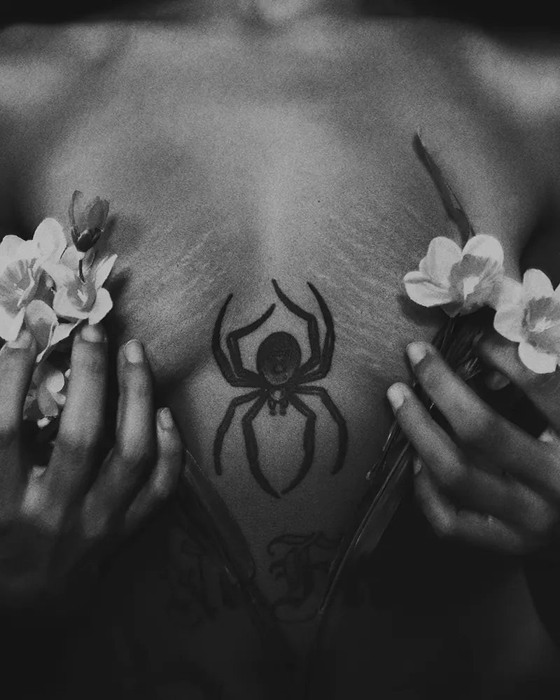 Black and white close-up photo of a woman’s breast with stretch marks, no bra, covered with flowers.