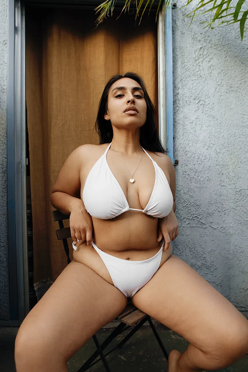 Color portrait of Sharon Clawson, plus-size Indian German woman in white bikini, thick thighs, big chest, visible cellulite and stretch marks, no makeup, natural beauty.