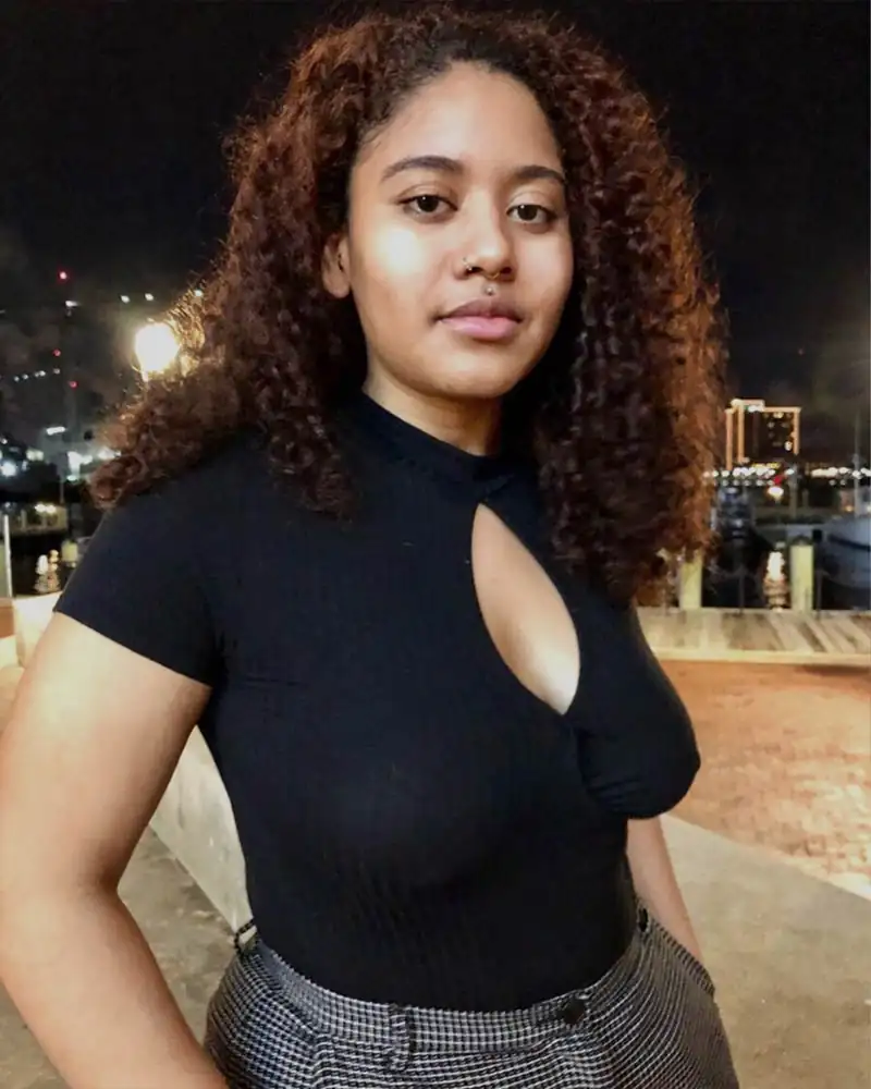 Black girl with curly hair wearing a black shirt, confidently posing and embracing her natural body.