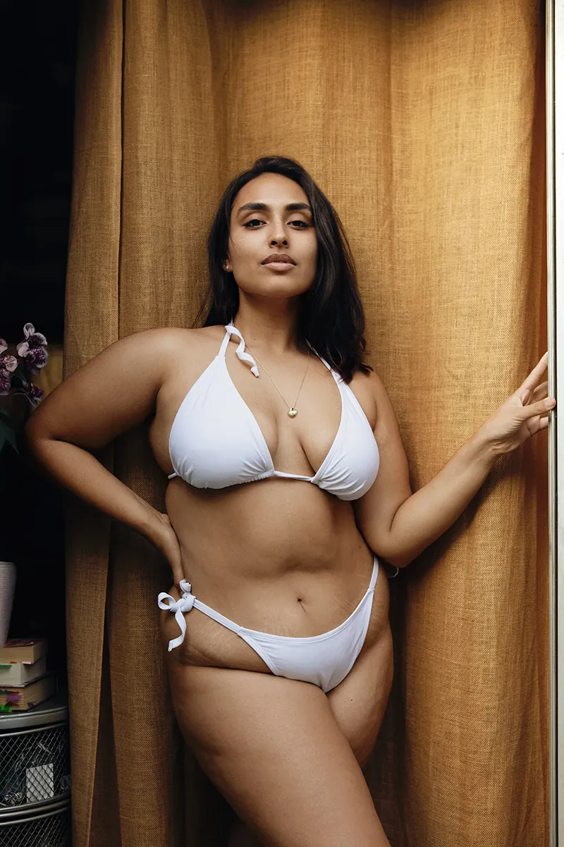 Sri Lankan plus-size model in a white bathing suit showing natural stretch marks and bare face, embracing her body with confidence and self-love.